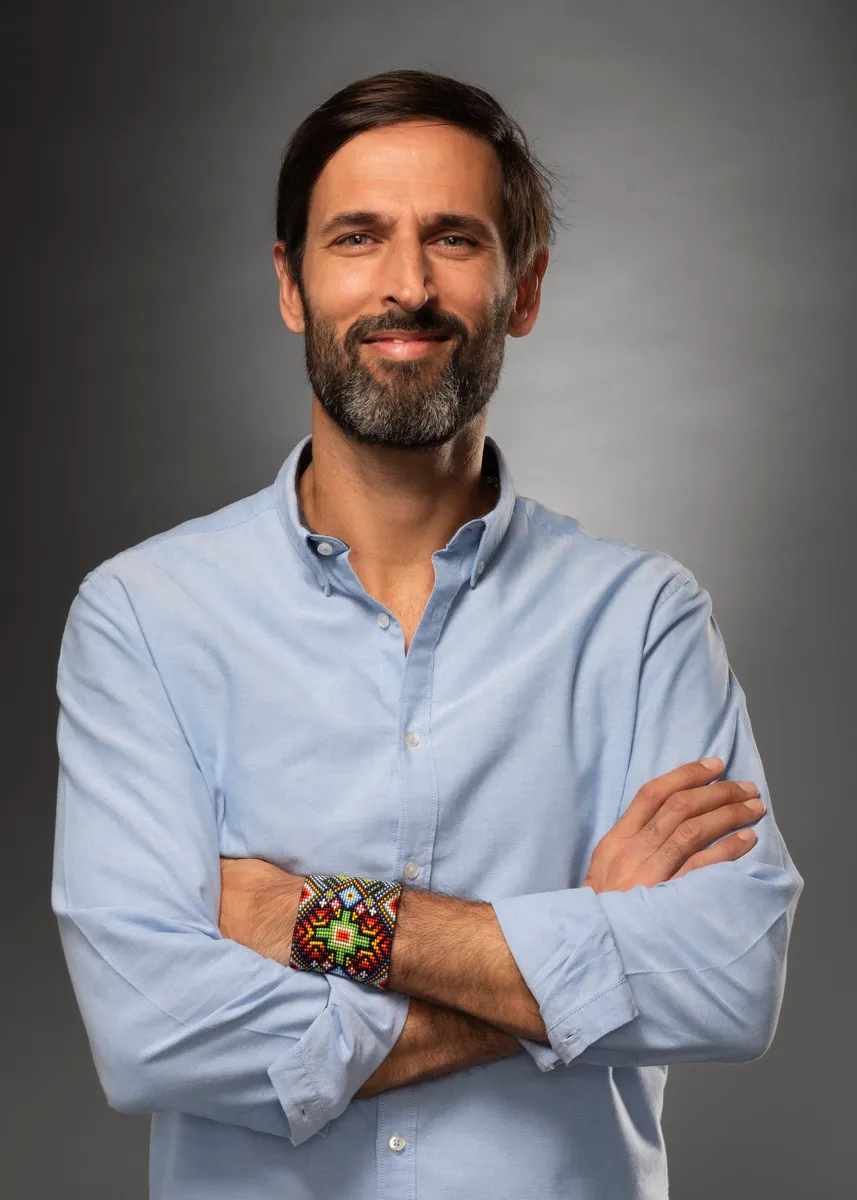 Portrait of Laurent Gheller, arms crossed, in a light blue shirt and a beaded bracelet.